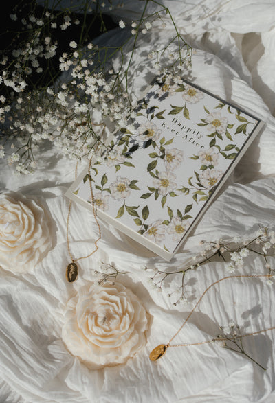 Floral box with 'Happily Ever After' text on a white fabric background with flowers and jewelry.